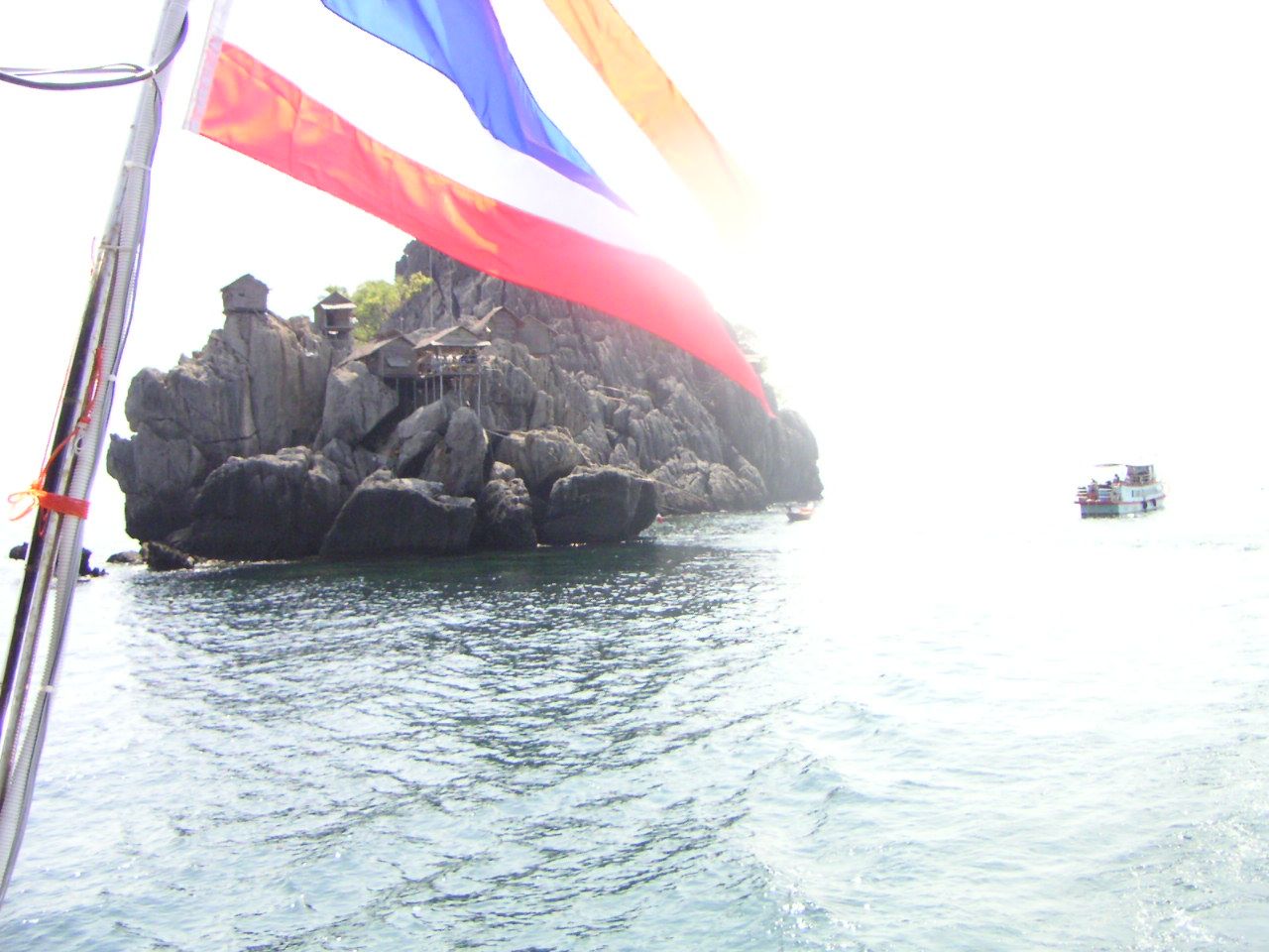 Une petite île rocheuse avec des structures construites dessus, entourée d'eau, et un drapeau thaïlandais visible au premier plan, en Thaïlande, photo gratuite