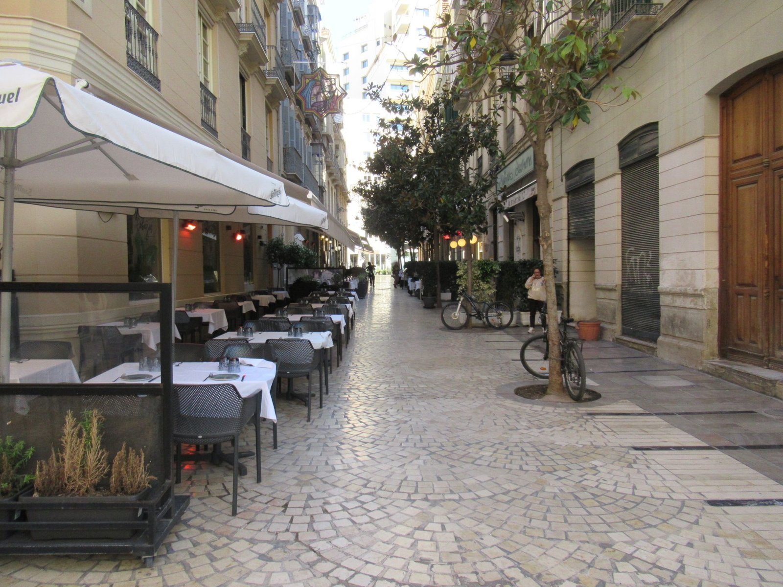 Ruelle pavée bordée d'immeubles, terrasse tables et chaises de restaurant installées sous des parasols à  Malaga, photo gratuite