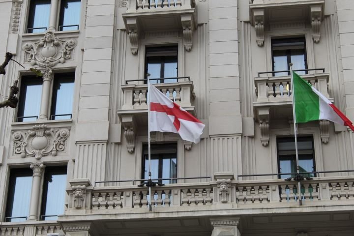Des drapeaux, Lombardie et Italie, accrochés sur un balcon orné d'éléments architecturaux classiques sur la façade d'un bâtiment, photo gratuite
