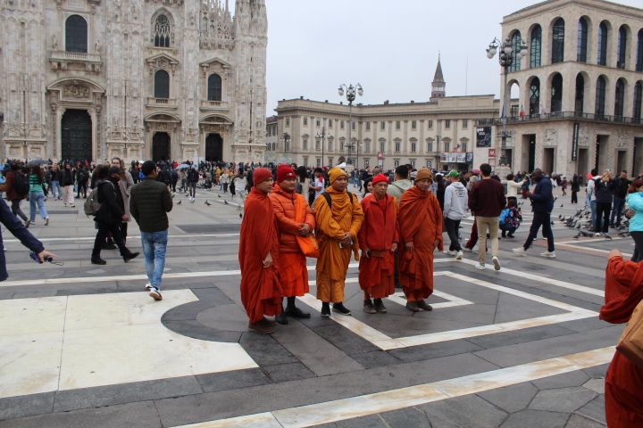 Groupe de moines tibétains vêtus de robes orange et rouges, devant la cathédrale de Milan Italie