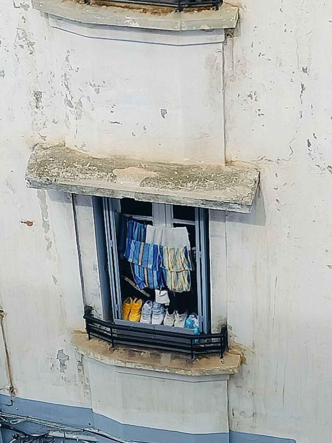 Paires de chaussures et vêtements suspendus pour sécher sur une fenêtre ouverte d’un bâtiment à façade blanche photo gratuite