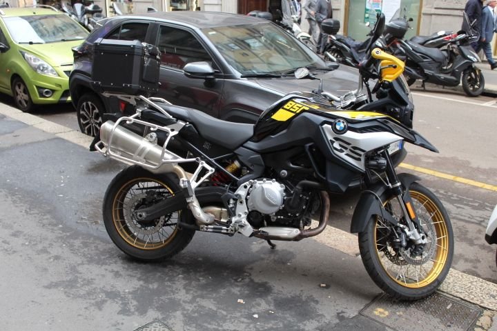 Une moto BMW F 850 GS ou une BMW F 850 GS Adventure garée au bord d'une ruelle de Milan, on y voit d'autres motos et des voitures, photo gratuite