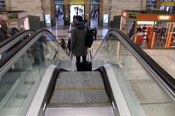 Personne habillée en noir, sac au dos, valise à la main, descendant un escalator dans un centre commercial dans la ville de milan Lombardie en Italie photo gratuite