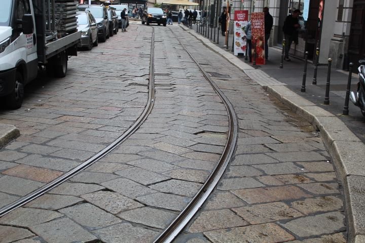 Une rue pavée de grandes dalles de pierre, des rails de tramway qui s'incurvent avec des voitures garées à côté, photo gratuite