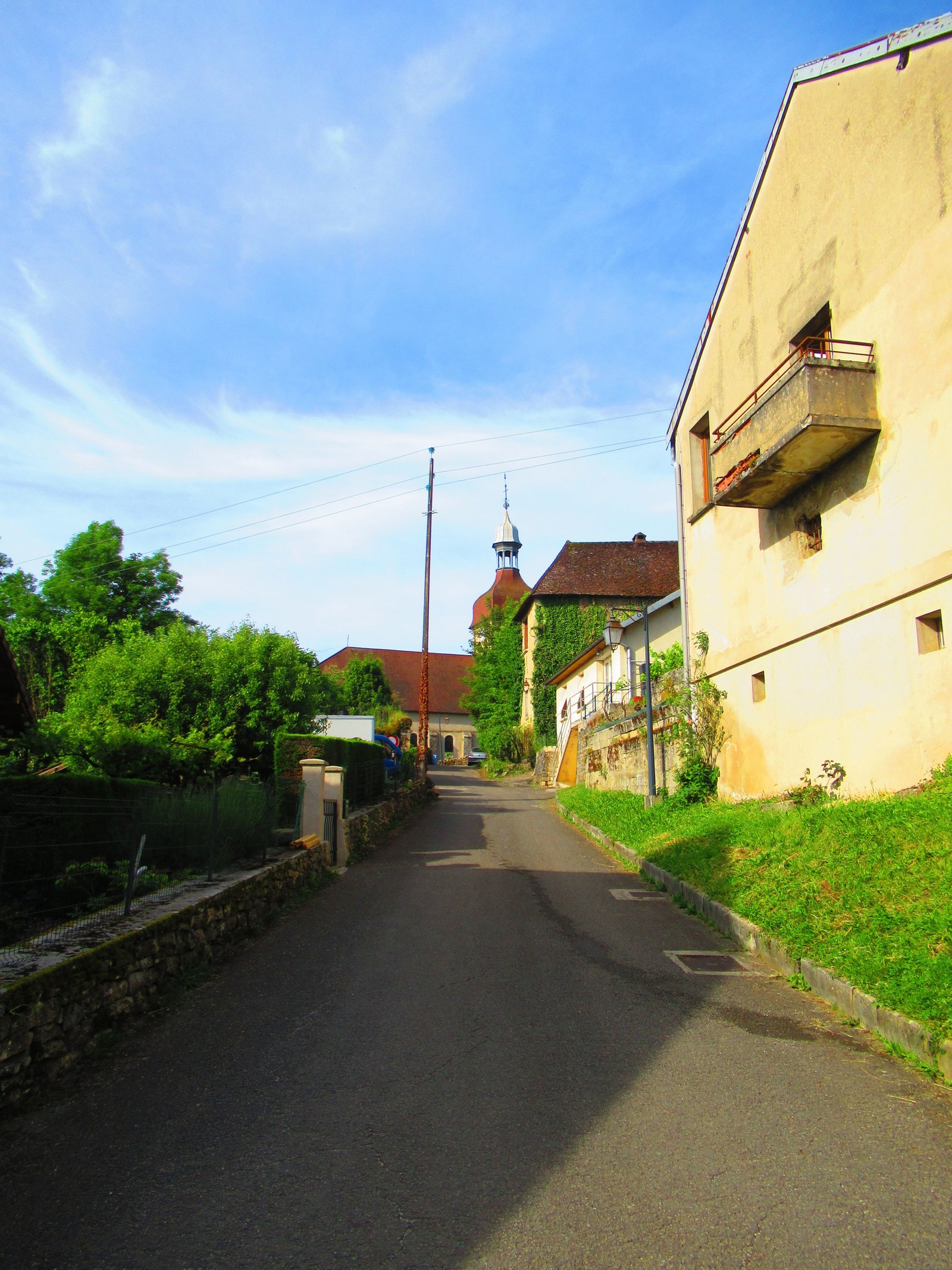 Une rue de village avec des maisons traditionnelles, de la végétation et un clocher d'église visible au loin, photo gratuite