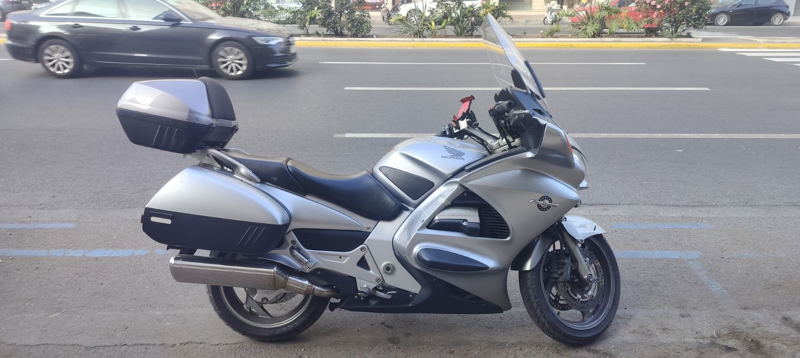 Une moto de marque Honda garée sur un trottoir - Uma moto da marca Honda estacionada num passeio, moto tipo touring na cor prata/cinza metalizado Foto gratuita