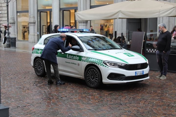 Une interaction entre un agent et une personne à côté d'une voiture de police de la Polizia Locale italienne, dans un environnement urbain, photo gratuite