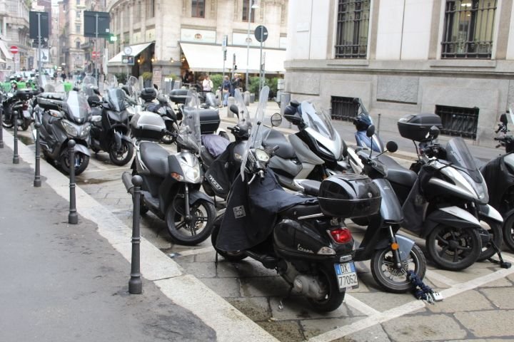 Un stationnement de scooters et de motos garés le long d'un trottoir dans une rue urbaine de Milan, photo gratuite