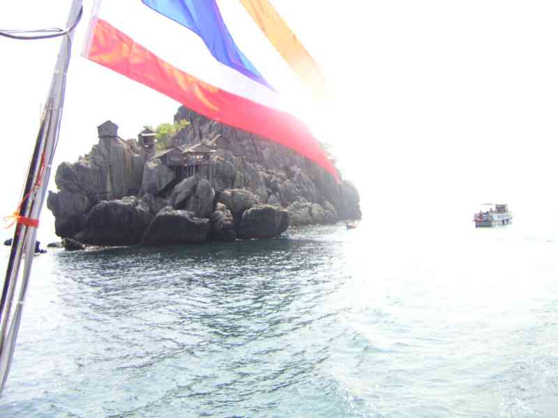 Une petite île rocheuse avec des structures construites dessus, entourée d'eau, et un drapeau thaïlandais visible au premier plan, en Thaïlande, photo gratuite