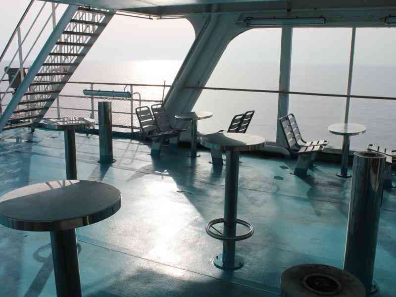 Le pont extérieur d'un bateau de croisière, avec des tables, des tabourets et des bancs, offrant une vue sur la mer, photo gratuite