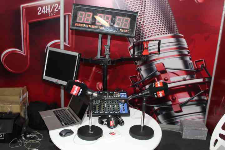 Un studio de radio ou d'enregistrement avec deux microphones, un ordinateur portable, un mélangeur audio, des écouteurs et un écran affichant l'heure, photo gratuite
