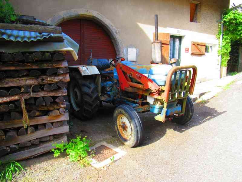 Un tracteur agricole garé près d'un bâtiment, à côté d'une pile de bois de chauffage