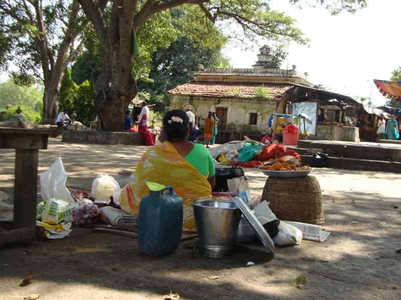 Une femme est assise par terre avec des marchandises à vendre, une vue des bâtiments traditionnels et d'autres personnes, photo gratuite