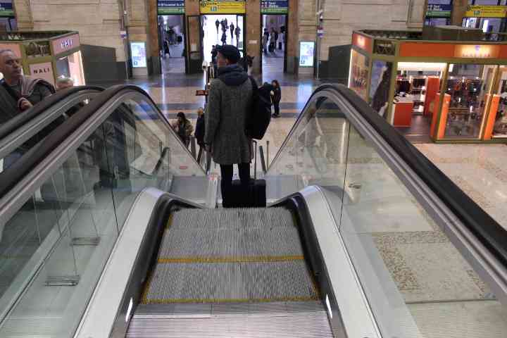 Personne habillée en noir, sac au dos, valise à la main, descendant un escalator dans un centre commercial dans la ville de milan Lombardie en Italie photo gratuite