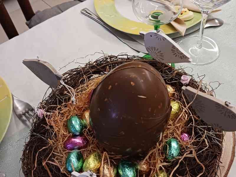 Une décoration de table festive centrée sur Pâques, avec un grand œuf en chocolat et de petits œufs colorés présentés dans un nid décoratif, photo gratuite