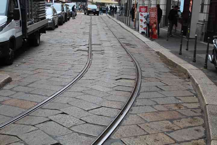 Une rue pavée de grandes dalles de pierre, des rails de tramway qui s'incurvent avec des voitures garées à côté, photo gratuite