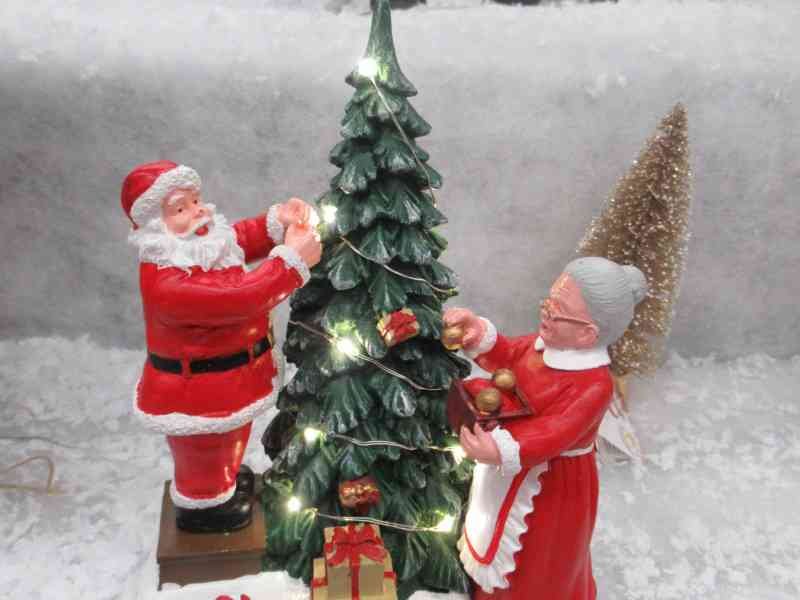 Une figurine représente le Père Noël et la Mère Noël décorant un sapin de Noël illuminé, photo gratuite